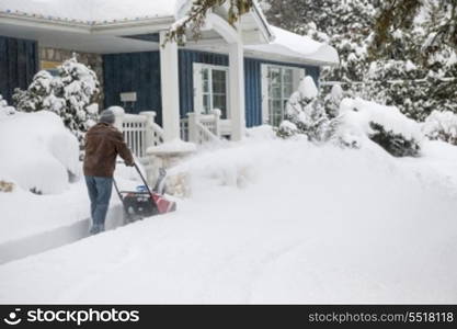 Man using snowblower in deep snow. Man using snowblower to clear deep snow on driveway near residential house after heavy snowfall