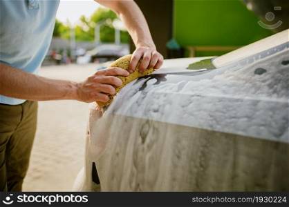 Man using sponge with foam, hand car wash station. Car-wash industry or business. Male person cleans his vehicle from dirt outdoors. Man using sponge with foam, hand car wash