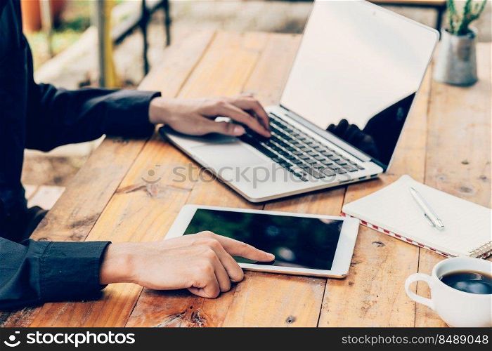 Man using tablet and laptop on table in coffee shop.