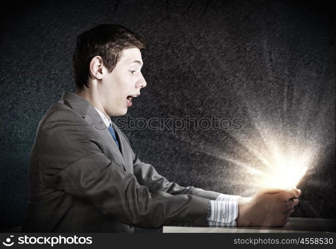 Man using tablet pc. Young emotional businessman looking shocked in tablet pc