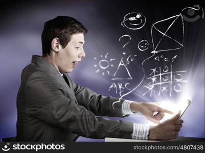 Man using tablet pc. Young emotional businessman looking shocked in tablet pc