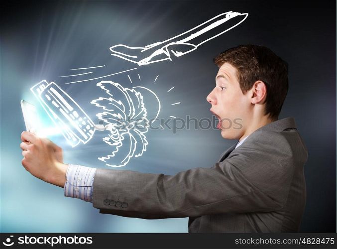 Man using tablet pc. Young emotional businessman looking shocked in tablet pc