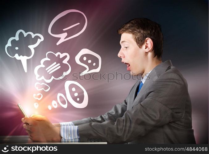 Man using tablet pc. Young emotional businessman looking shocked in tablet pc