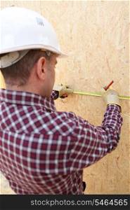 Man using tape measure to mark wooden panel