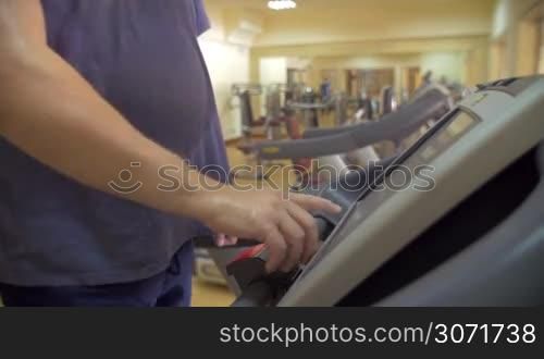 Man using treadmill in the gym. He using touchscreen control panel to change options and then to turn off the exercise machine
