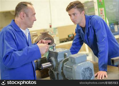 Man using wrench on machine, apprentice watching