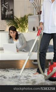 Man vacuuming and woman laid with laptop