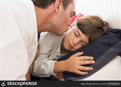 Man waking young boy in bed with kiss