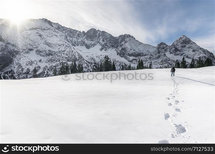 Man walking alone through the snow towards the snow-capped Alps mountains, near Ehrwald, in Austria, on a sunny day. Footsteps path in the snow.