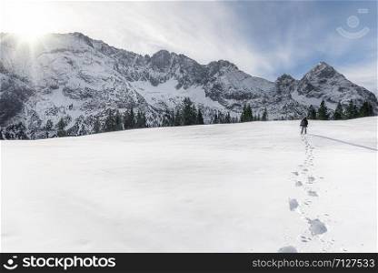 Man walking alone through the snow towards the snow-capped Alps mountains, near Ehrwald, in Austria, on a sunny day. Footsteps path in the snow.