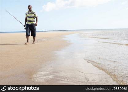 Man Walking Along Shore Of Beach Carrying Fishing Rod