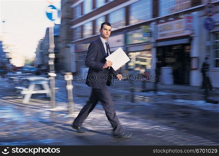 man walking in city street carrying a document