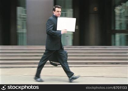 man walking in city street holding sign or document