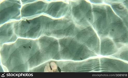 Man walking in crystal clear sea water of Sardinia, Italy. View of male feet underwater on white sand