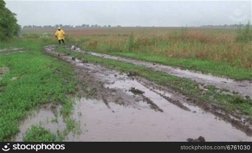 Man walking on muddy dirt road with puddles through the field in rain