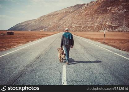 man walking on the road with his dog in the mountains