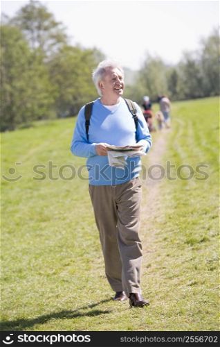 Man walking outdoors holding map smiling with people in background