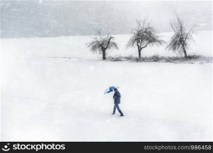 Man walking through bad winter snowstorm, on a cold day of January, in Germany. Winter bad weather scenery. Strong snowfall and windy day.