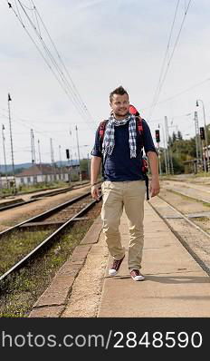 Man walking towards train station backpack travel railroad smiling tourist