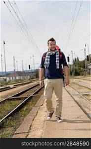 Man walking towards train station backpack travel railroad smiling tourist