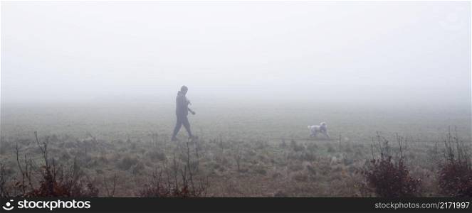 man walks dog on field in winter mist near utrecht in the netherlands