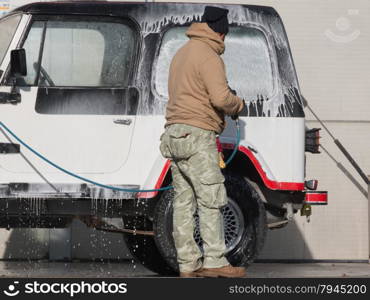 Man washing his car with a jet of water and shampoo