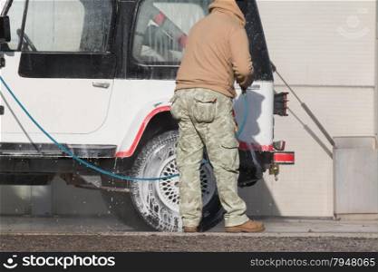 Man washing his car with a jet of water and shampoo