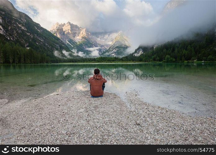 Man watching cloudy sunrise at the mountain lake