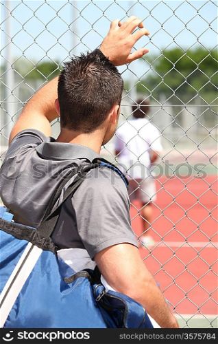 Man watching friend play tennis