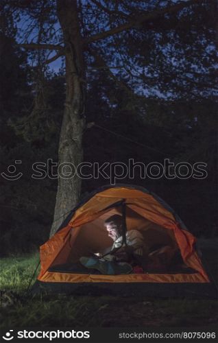 Man watching his smartphone in a tent at night.