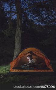 Man watching his smartphone in a tent at night.