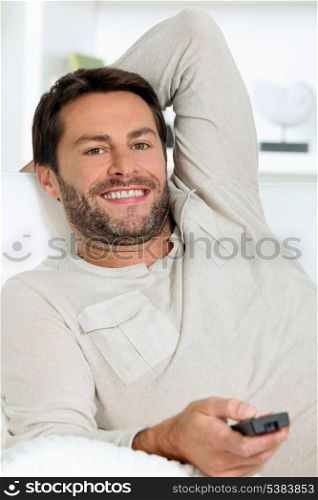 Man watching television in a white room using a remote control