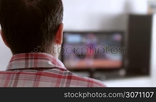 Man watching television in living room. Shot from behind.