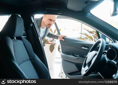 Man watching the interior of new car in showroom. Male customer choosing vehicle in dealership, automobile sale, auto purchase. Man watching the interior of new car in showroom