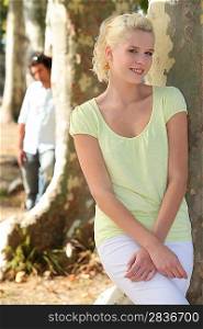 Man watching woman leaning on tree trunk