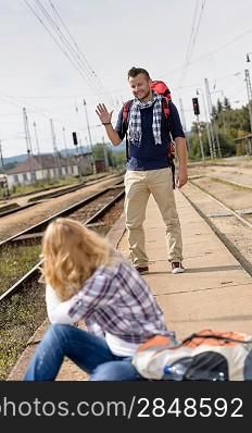Man waving to woman sitting on railroad vacation travel backpack