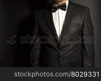 man wearing a black suit and bow tie on black background
