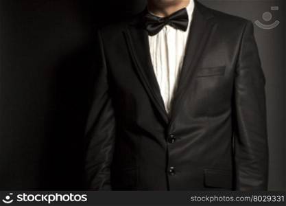 man wearing a black suit and bow tie on black background
