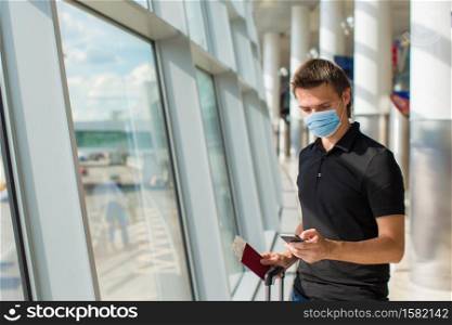 Man wearing a mask for prevent virus in international airport lounge waiting for flight aircraft. Protection against Coronavirus and gripp. Young man in an airport lounge waiting for flight aircraft.