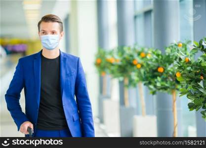 Man wearing a mask for prevent virus in international airport lounge with his luggage. Protection against Coronavirus and gripp. Young man in an airport lounge waiting for flight aircraft.