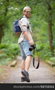 man wearing backpack walking in a forest holding dslr camera