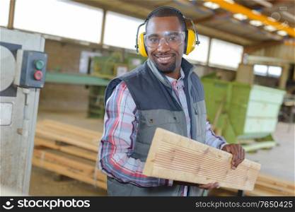 Man wearing earmuffs holding plank of wood