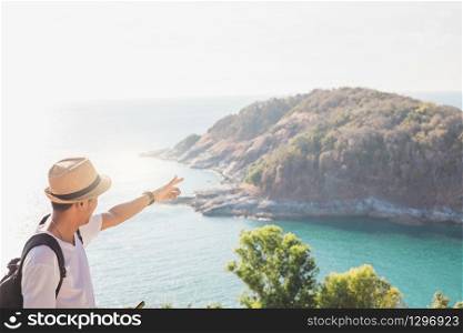 Man wearing hat holds his hand happy. Man asian tourist Look at mountains and the sea Before sunset.for activity lifestyle outdoors freedom or travel tourism inspiration backpacker tourist to covid 19