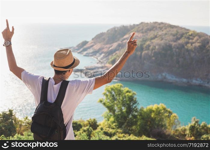 Man wearing hat holds his hand happy. Man asian tourist Look at mountains and the sea Before sunset.for activity lifestyle outdoors freedom or travel tourism inspiration backpacker tourist to covid 19