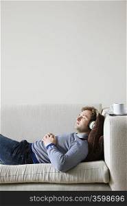 Man wearing headphones lying on sofa in living room, side view