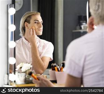man wearing make up using foundation looking into mirror
