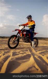 Man wearing protective helmet and suit on sport motor over sand dune terrain track. Motocross driver. Man on sport motor over sand terrain