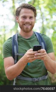 man wearing rucksack using smartphone in the countryside