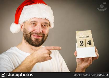 Man wearing santa claus christmas hat holding calendar with 24 december date, on grey. December 24th. Man santa hat holds calender