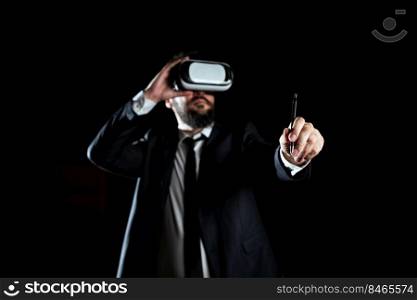 Man Wearing Virtual Reality Simulator Holding Pen During Training.. Male Professional Wearing Virtual Reality Goggles Holding Pen And Presenting Modern Technology Of Learning. Businessman Wearing Suit Taking Training Through Simulator.